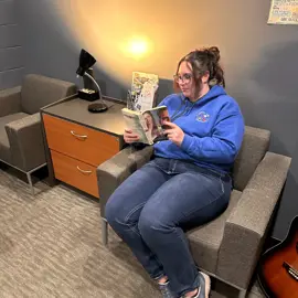 woman in chair reading book by lamp and side table