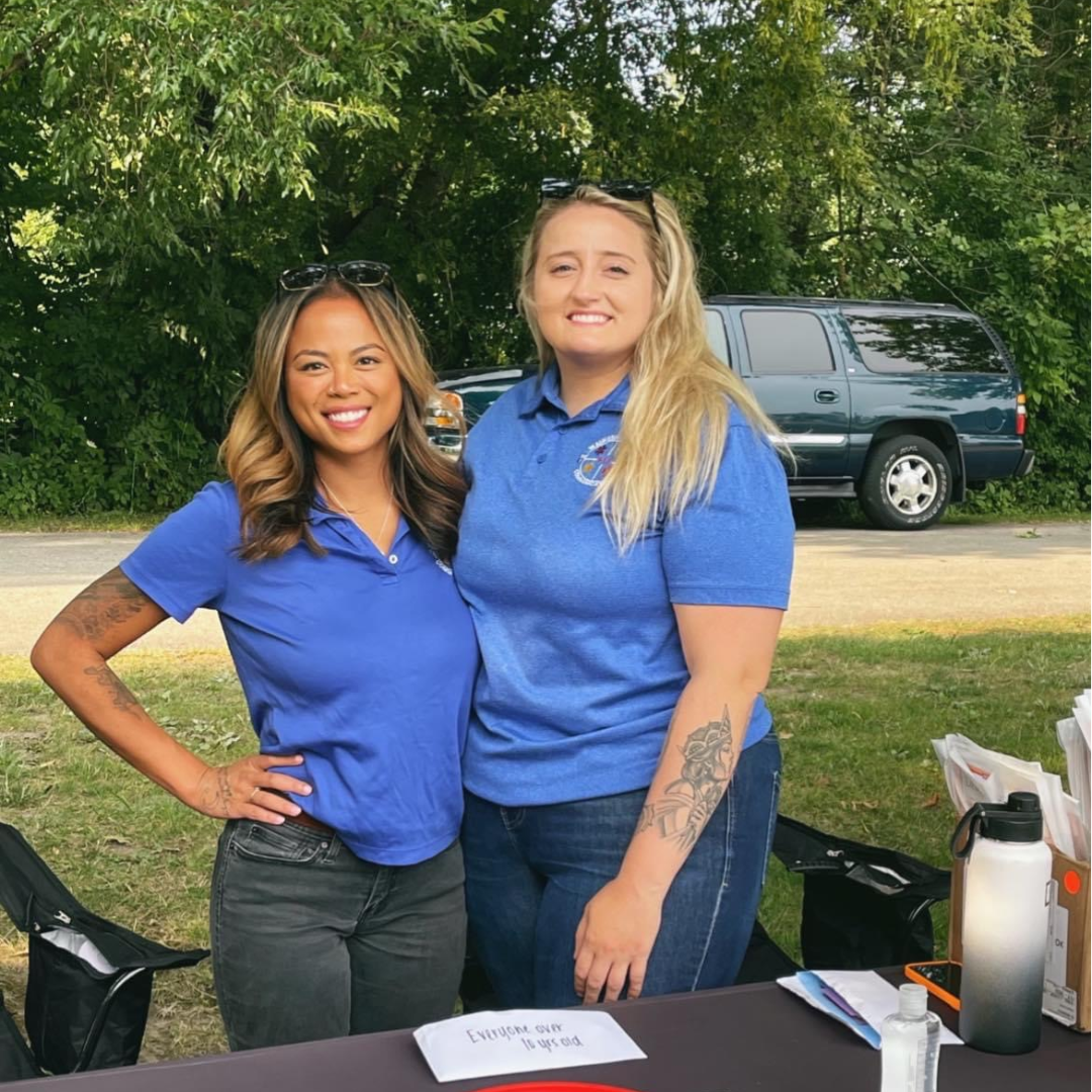 two females in blue uniform shirts at an outdoor community event speaking to the public about 9-1-1