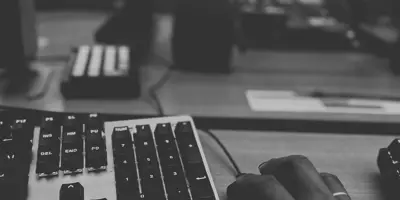 black and white photo of hand on mouse next to keyboard and in front of computer screens